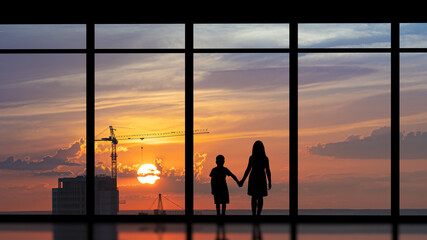 Fototapeta na wymiar The boy and girl standing near the panoramic window against the city sunset
