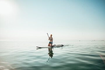 Woman standing firmly on inflatable SUP board and paddling. Hands pushing and pulling the paddle through shining water surface and propelling paddleboard on sunny morning