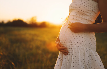 Close-up of pregnant woman with hands on her belly on nature.