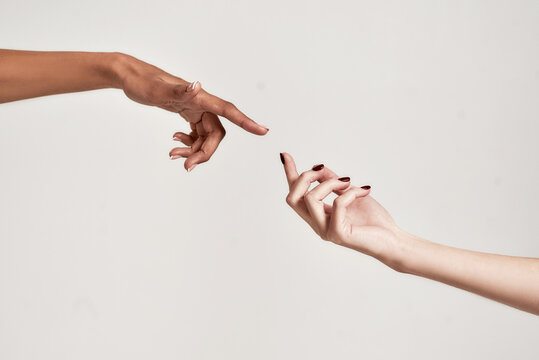 Close up of two hands of diverse women reaching for each other isolated over grey background