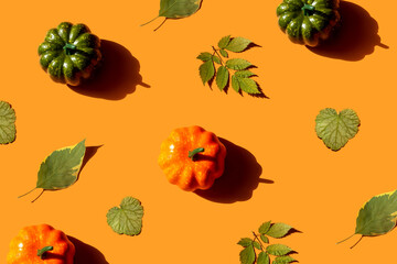 Autumn flat lay with various pumpkins and dried leaves on orange background, top view. Halloween and autumn concept, greeting card.