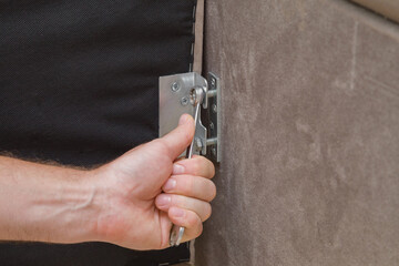 Young man hand using wrench and screwing screw in metal steel angle connector in corner of bed. Putting together parts of sofa. Assembling new textile furniture. Closeup.