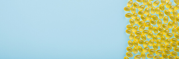 Fish oil capsules on light blue table background. Pastel color. Yellow nutritional supplements wide banner. Medical, pharmacy and healthcare concept. Empty place for text or logo. Closeup. Top view.