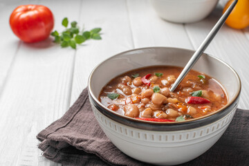 Bulgarian Soup Bob Chorba whith been, tomatoes, bread and mint on white wooden table. Horizontal orientation. Close up.