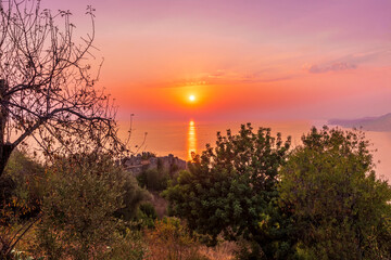 scenic view at picturesque sunset from high mountain with bushes and green trees below and beautiful cloudy sky, sea with far coast, sun glow with reflection on the background , castle landscape