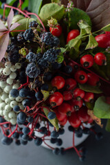 Autumn bouquet of berries, fruits and leaves in a light ceramic vase on a dark background.