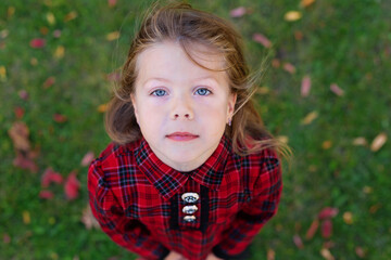 A beautiful girl with blue eyes looks up. Child in a red autumn dress. View from above. Camera from above. Looks at the sky. Autumn theme