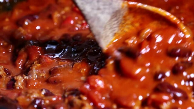 Cooking chili con carne in a frying pan. The bean stew is boiling.