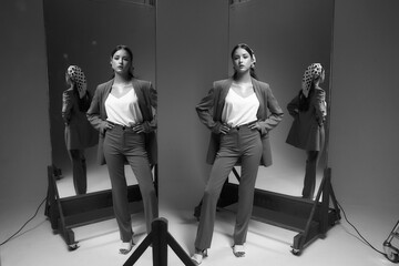 Elegant fashionable woman in brown suit, sabot shoes and polka dot kerchief standing and posing in studio on gray background between mirrors. Fashion portrait with reflections. Beautiful teenager girl