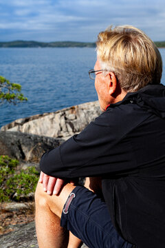 Senior blonde man sitting on a hill looking out at the sea on a warm autumn day