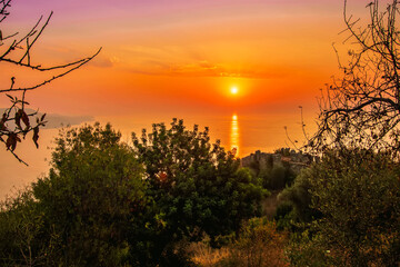 scenic view at picturesque sunset from high mountain with bushes and green trees below and beautiful cloudy sky, sea with far coast, sun glow with reflection on the background , castle landscape