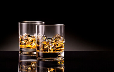 Two glasses of whiskey with ice cubes on black background.