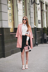 sexy young stylish beautiful woman walking in street, wearing pink coat, purse, sunglasses, white shirt, black skirt, fashion outfit, autumn trend, smiling happy, accessories