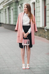 Obraz premium attractive stylish smiling woman walking city street in pink coat spring fashion trend holding purse, elegant style