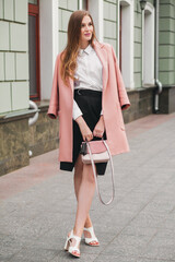 attractive stylish smiling woman walking city street in pink coat spring fashion trend holding purse, elegant style