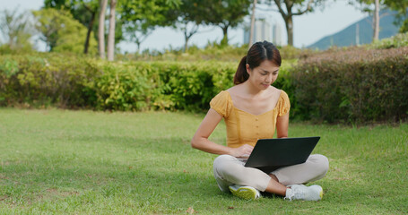 Woman work on laptop computer and sit on green lawn