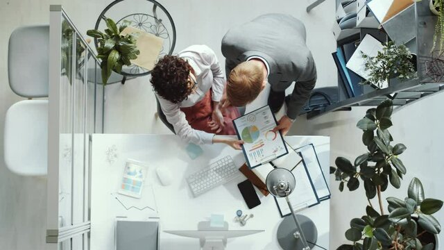 Time lapse top down shot of businesswoman typing on computer, talking with colleagues, taking notes, using digital tablet and signing documents while working at desk in office