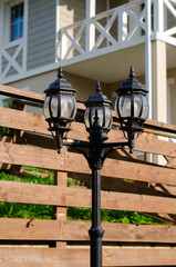 Lantern on the background of a wooden fence near the house in the cottage village. Vertical photo.