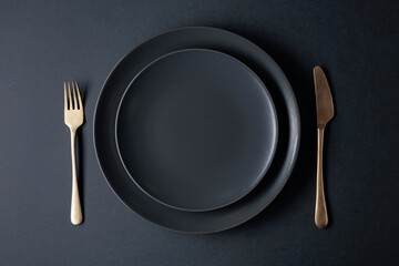 Empty black plate, fork and knife on a black background. Top view.