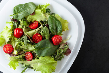 Fresh mixed salad with cherry tomatoes on a black background. Top view.