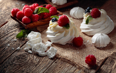 Dessert Pavlova with raspberries, blueberries and mint on a old wooden table.
