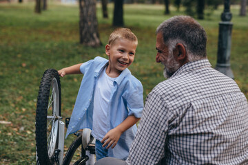 grandfather with his grandson at the city park fixing bicycle