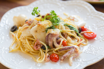 The spaghetti seafood, contained  squid,bacon and tomatoes, with white sauce in a white dish.