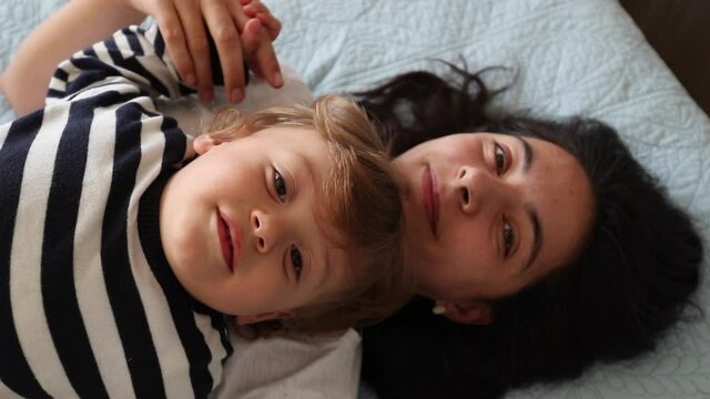 Mother and child toddler lying in bed together smiling at camera