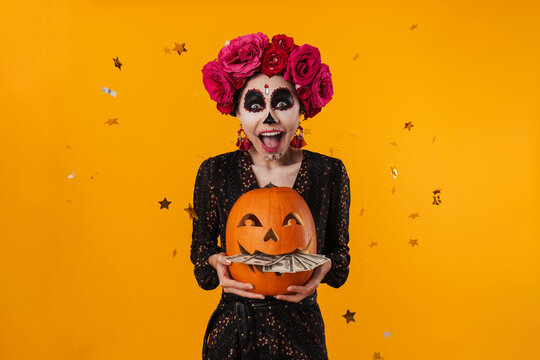 Photo of girl in halloween makeup posing with pumpkin and dollars