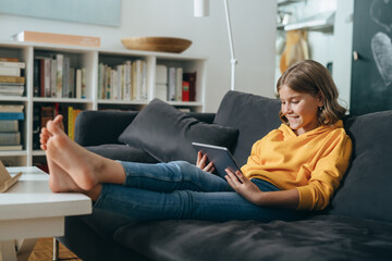 young girl sitting on sofa and using tablet computer at her home