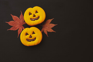 Funny Halloween jack o lantern pumpkin cookies and dry autumn leaves.