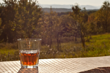 Glass with drink on a background of greenery and nature. Whiskey on an old wooden board. Sunny summer day. Mockup for design. Copy space and place for products.