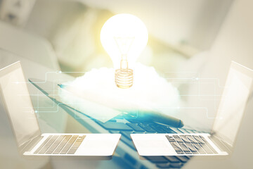 Computer on desktop in office with bulb icon hologram. Double exposure. Concept of idea.