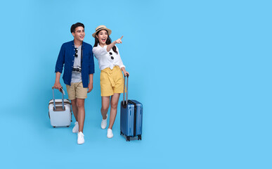 Happy Asian couple tourist hand pointing to copy space with baggage going to travel on holidays isolated on blue background.