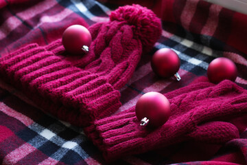 Obraz na płótnie Canvas beautiful, warm, cozy, knitted red set: a hat with a pompom and mittens lie on a checked scarf. Winter, Christmas, cute and useful, gifts. Knitted set as a gift