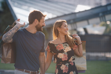 A young couple in love returns from shopping and carry shopping bags with them, holding hands and walking together