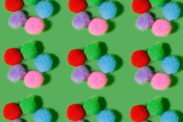 Pattern. Fluffy balls of different colors on a green background. Multicolored balls of thread lie in the shape of a flower. Bright cheerful background.