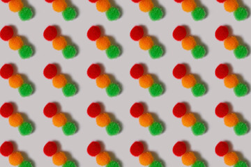 Pattern. Fluffy red, yellow and green balls on a white background. Multi-colored balls of thread lie in rows. Bright cheerful background.
