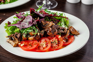 Mushroom and tomato salad dressed with pesto sauce and pine nuts. Serving food in a restaurant on a white plate.