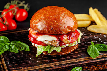 American cuisine. Burger with chicken, cheese, tomatoes, lettuce and tomato sauce. Serving the dish on a wooden board.