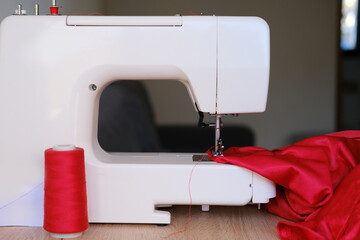 red velvet cloth, threads lie at modern sewing machine, selective focus on needle and moving parts of technology, hobby and needlework concept, textile production