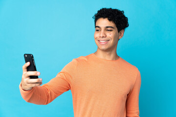 Venezuelan man isolated on blue background making a selfie with mobile phone