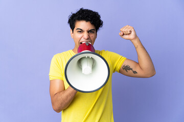 Young Venezuelan man isolated on purple background shouting through a megaphone to announce...