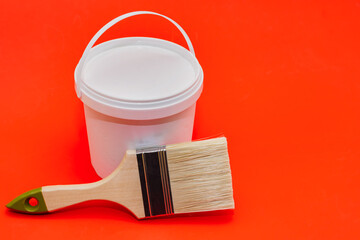 Renovation concept. Plastic jar with paint and brush on a red background