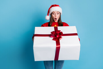 Photo of cute pretty lady hold look big white decorated box open mouth shocked expression wear santa x-mas headwear red ornamented pullover jeans isolated blue color background