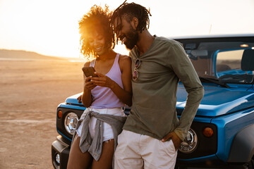Image of joyful african american couple using mobile phone while travelling with car