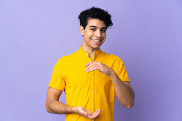 Young Venezuelan man isolated on purple background holding copyspace imaginary on the palm to...