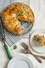 Top down view of vegetarian spinach and feta filo pastry pie with one piece cut out, white background top down view