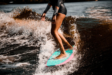 view on tanned legs of woman riding wave on surf style wakeboard
