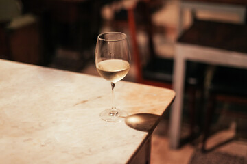 A glass of white wine on a marble table in a dark bar